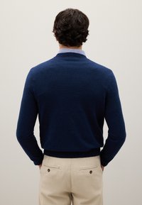 Maglione a maglia blu navy con maniche lunghe e scollo rotondo, abbinato a pantaloni beige chiaro con due tasche posteriori e bottoni a contrasto.