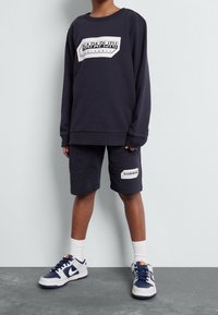 Set di felpa e pantaloni corti in cotone di colore navy. La felpa presenta un'etichetta logo bianca; i pantaloni corti hanno dettagli simili. Abbinati a sneakers bianche e navy.