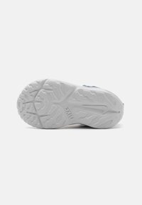Semelle de chaussure de sport blanche avec un motif de tread texturé. Le design présente des courbes et des crêtes pour une meilleure adhérence. Matériau durable avec des détails de logo.