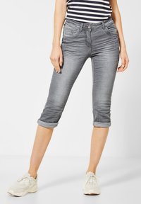 Vaqueros capri de mezclilla gris con dobladillos enrollados, que presentan un corte ajustado, cinco bolsillos y un sutil efecto de desvanecimiento. Combinados con zapatillas blancas.