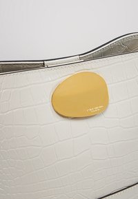 Borsa in pelle goffrata a coccodrillo bianca con una raffinata fibbia ovale dorata liscia con marchio in rilievo. Cuciture lineari lungo i bordi.