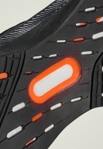 Suola di scarpa sportiva nera con gomma testurizzata, dotata di un inserto "Torsion System" bianco e arancione e scanalature a motivo per una migliore aderenza.