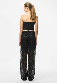 Črni kratki vrh s tankimi naramnicami, združen z prozornimi črnimi čipkastimi hlačami z rožnatimi vzorci in elastičnim pasom.