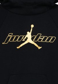 Melnā kapuce ar lielu zelta "Jordan" logotipu ar lēkjošu figūru. Mīksts audums ar priekšējo kabatu un kapuci ar auklu.