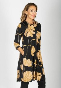 Czarna sukienka z dużymi beżowymi wzorami kwiatowymi, z kołnierzykiem, długimi rękawami i kieszeniami; zwiewny materiał i fason do kolan.