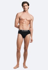 Black cotton briefs with a white "ALLSAINTS" logo on the waistband, featuring a snug fit and smooth texture. Model displays body shape.