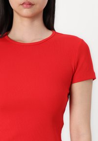 Top rouge à rayures, à manches courtes, avec un col rond, une texture lisse et une coupe ajustée, soulignant une silhouette près du corps.