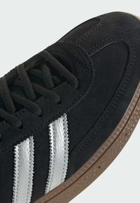 Baskets en daim noir avec un motif à trois bandes argentées, lacets noirs et semelle en caoutchouc marron texturée. Présente des accents cousus et un bout rond.