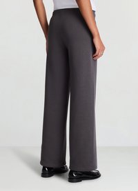 Pantaloni grigi a gamba larga con una texture liscia e fascia elastica in vita, abbinati a scarpe nere. La vista mostra i dettagli posteriori e laterali.