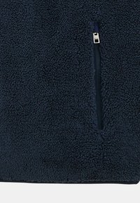 Pull-over en polaire bleu marine avec une surface douce et texturée et une poche zippée sur le devant. Présente un design uni sans motifs visibles.