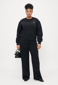 Sweatshirt noir surdimensionné avec des poignets et un ourlet côtelés, associé à un pantalon noir à jambes larges. Les accessoires comprennent un petit sac à main noir.