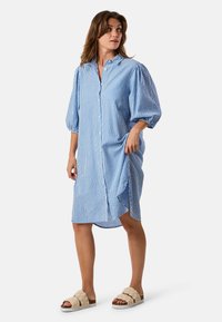 Abito camicia a righe blu e bianche con bottoni frontali, maniche a palloncino morbide e tasche laterali. Tessuto morbido con vestibilità rilassata.