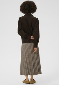 Veste en velours côtelé brun avec un col, associée à une jupe midi à carreaux dans des tons neutres et des chaussures plates en brun clair.