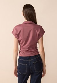 Kortermet topp i plommefarge med en tettsittende design, rynkedetalj i midjen, kombinert med mørkeblå denimbukser med baklommer.