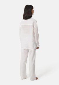 Camicia di lino bianca e pantaloni larghi abbinati, caratterizzati da una vestibilità comoda, maniche lunghe e una sottile texture trasparente. I pantaloni sono in stile wide-leg.