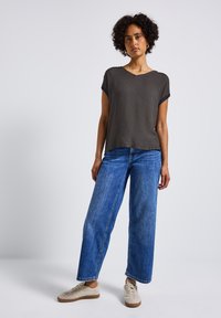 Haut gris à manches courtes avec une texture à motifs, associé à un jean en denim bleu ample et des baskets de couleur claire. Tenue simple et décontractée.