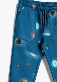 Blauwe joggingsbroek met een ruimteprint van planeten, sterren en asteroïden. Gemaakt van zachte stof met een elastische tailleband en zakken.