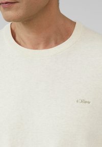 Helle beige Strickjacke mit Rundhalsausschnitt, ausgestattet mit gerippten Kanten und einem gestickten s.Oliver Logo in einem etwas dunkleren Beige.