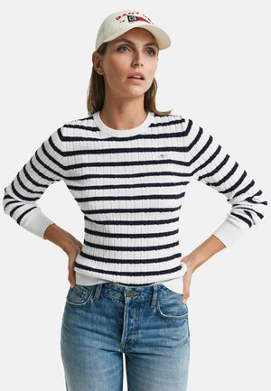 Striped sweater in white and navy with a ribbed texture, featuring a round neckline and fitted silhouette, worn with blue jeans.