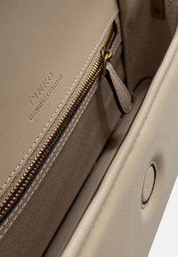 Interno di una borsa in pelle beige con una cerniera dorata e logo del marchio in rilievo. Texture liscia con cuciture a contrasto.
