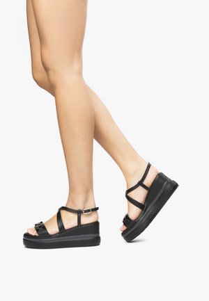 Schwarze Plateausandalen mit verstellbaren Knöchelriemen, glatter Oberfläche, offenem Zehendesign und rutschfester Sohle.