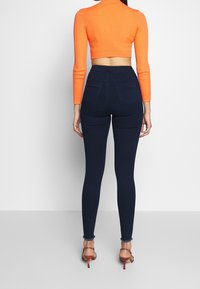 Vaqueros ajustados de talle alto en azul oscuro con una textura suave, combinados con un top corto acanalado de color naranja brillante con mangas largas.