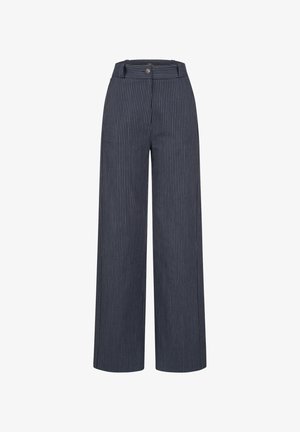 Mujer con pantalones anchos a rayas en azul marino con botón y cremallera, combinados con sandalias negras de punta abierta y una camiseta blanca.