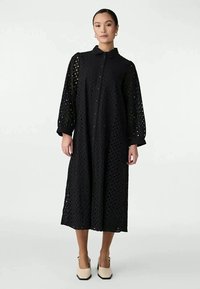 Vestido preto de manga longa com design perforado, frente com botões e colarinho, comprimento até à meia-coxa e corte solto.