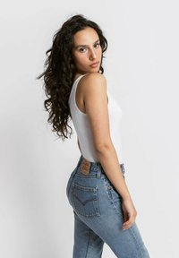Canotta bianca e jeans blu in denim a vita alta con un'etichetta in pelle marrone sul retro, caratterizzati da un classico design a cinque tasche e dettagli di cucitura.