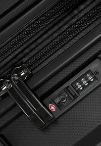 Valigia nera caratterizzata da un materiale texturizzato, doppia cerniera, meccanismo di blocco e una combinazione approvata dalla TSA con dettaglio in rosso.