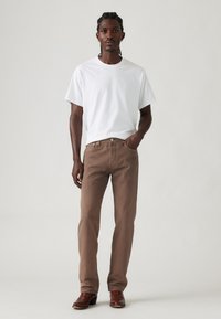 Brune bomuldsbukser og en hvid t-shirt med korte ærmer, stående figur, med brune læderstøvler, neutral baggrund. Enkel design, ingen mønstre.