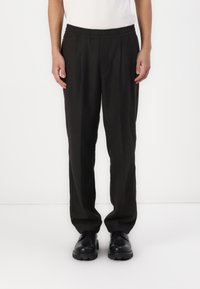 Pantalons noirs à coupe décontractée avec une taille élastique, en tissu lisse et à coupe droite, associés à des chaussures noires.
