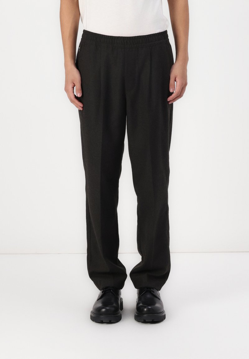 Pantalons noirs à coupe décontractée avec une taille élastique, en tissu lisse et à coupe droite, associés à des chaussures noires.