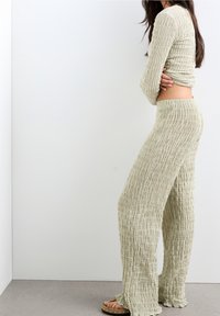 Tweedelig set in lichtgroen, met een textuurstof en een gekreukt ontwerp. Langarmige top en wijde broek, gecombineerd met platte sandalen.