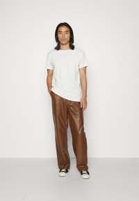 T-shirt blanc à col rond associé à un pantalon en cuir marron avec poches latérales et coupe décontractée. Des baskets noir et blanc complètent le look.