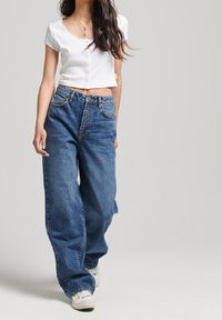 Bílé zkrácené košilové tričko s krátkým rukávem, spárované s volnými modrými džínami a bílými teniskami. Jednoduchý design, ležérní střih.