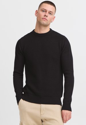 Black knit sweater with a textured ribbed design, crew neckline, and long sleeves. Features a fitted waistband and cuffs for structure.