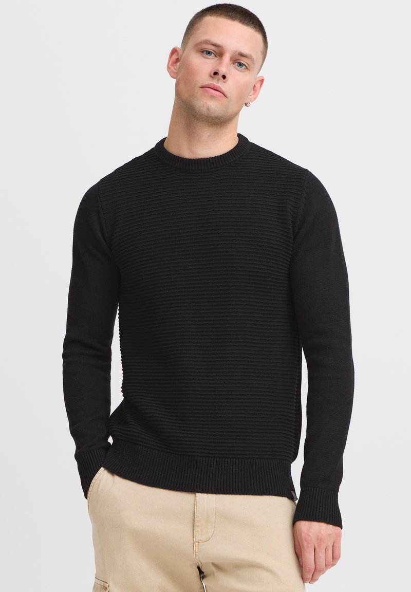 Zwarte gebreide sweater met een textuur en ribbelontwerp, ronde halslijn en lange mouwen. Bevat een aansluitende tailleband en manchetten voor structuur.