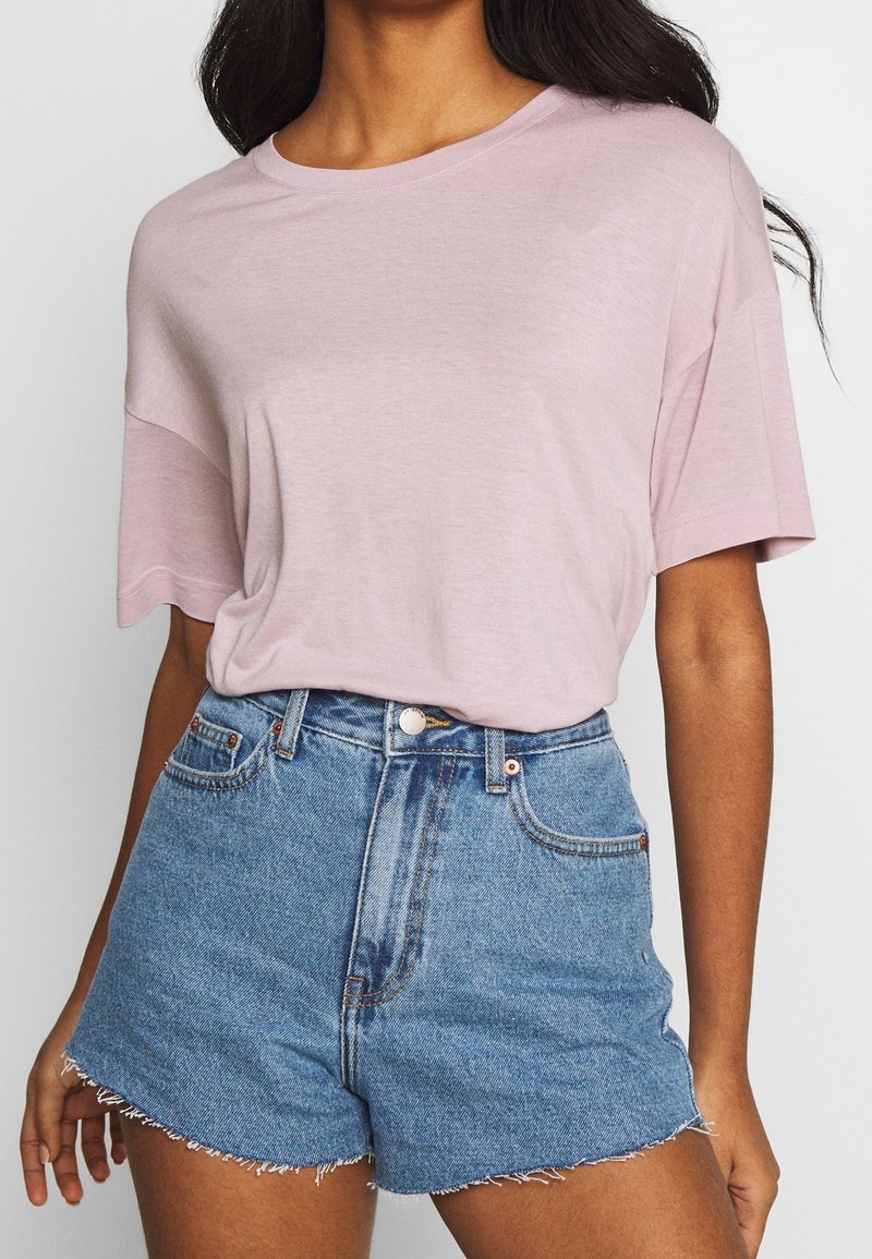 Lichtroze, T-shirt met korte mouwen van zacht materiaal, gecombineerd met hoogwaisted denim shorts met rafelige zomen en een klassieke blauwe was.