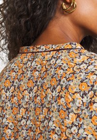 Blomstret bluse med en mørk baggrund og orange og lyseblå blomster. Letvægtsstof med en diskret struktur og en rund halsudskæring.