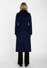 Marineblauer Wollmantel mit maßgeschneidertem Design, langen Ärmeln und geradem Schnitt, kombiniert mit schwarzen Hosen mit weitem Bein.