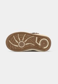 Vista inferior de un zapato que presenta una suela de goma marrón con un intrincado patrón de tracción y acentos en blanco sucio.