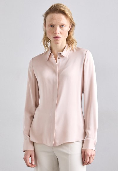 Blouse rose clair à manches longues en tissu lisse, avec un devant boutonné, un col et une légère brillance. Coupe ajustée avec un ourlet arrondi.