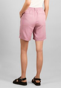 Rosa bomullsshorts med elastisk midjebånd og to baklommer. Lengden når midt på låret. Kombinert med svarte sandaler med stropper.
