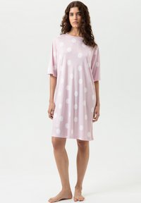 Robe de nuit en coton rose à pois blancs, manches courtes, coupe ample, encolure arrondie, et ourlet à hauteur du genou. Texture douce.