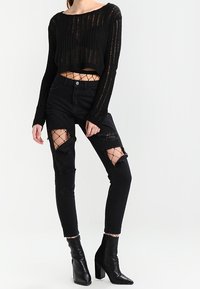 Černý zkrácený pletený svetr s dlouhými rukávy, kombinovaný s černými roztrhanými skinny džíny se síťovinovými detaily, doplněný černými lodičkami na kotníky.