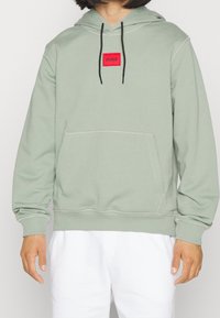 Felpa verde chiaro in misto cotone, con tasca frontale, laccetti neri e un'etichetta rossa al centro del petto.