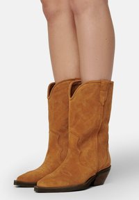 Bottes de cowboy en daim d'une couleur tan chaude, avec des bouts pointus, des coutures décoratives et des talons robustes, dotées de poignées sur les côtés pour un enfilage facile.