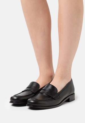 Schwarze Lederloafers mit einem niedrigen Absatz weisen ein gesticktes Design und einen dekorativen Riemen an der Vorderseite auf. Glatte Textur mit minimalen Akzenten.