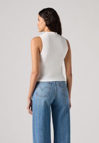 Sleeveless white top made of soft material, fitted design. Paired with loose, light blue denim jeans featuring two back pockets.